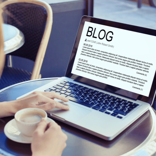 A person sits at a round table with a cup of coffee, reading a blog post on business coaching for therapists displayed in large text on their laptop screen. | Stresslesstherapist.com